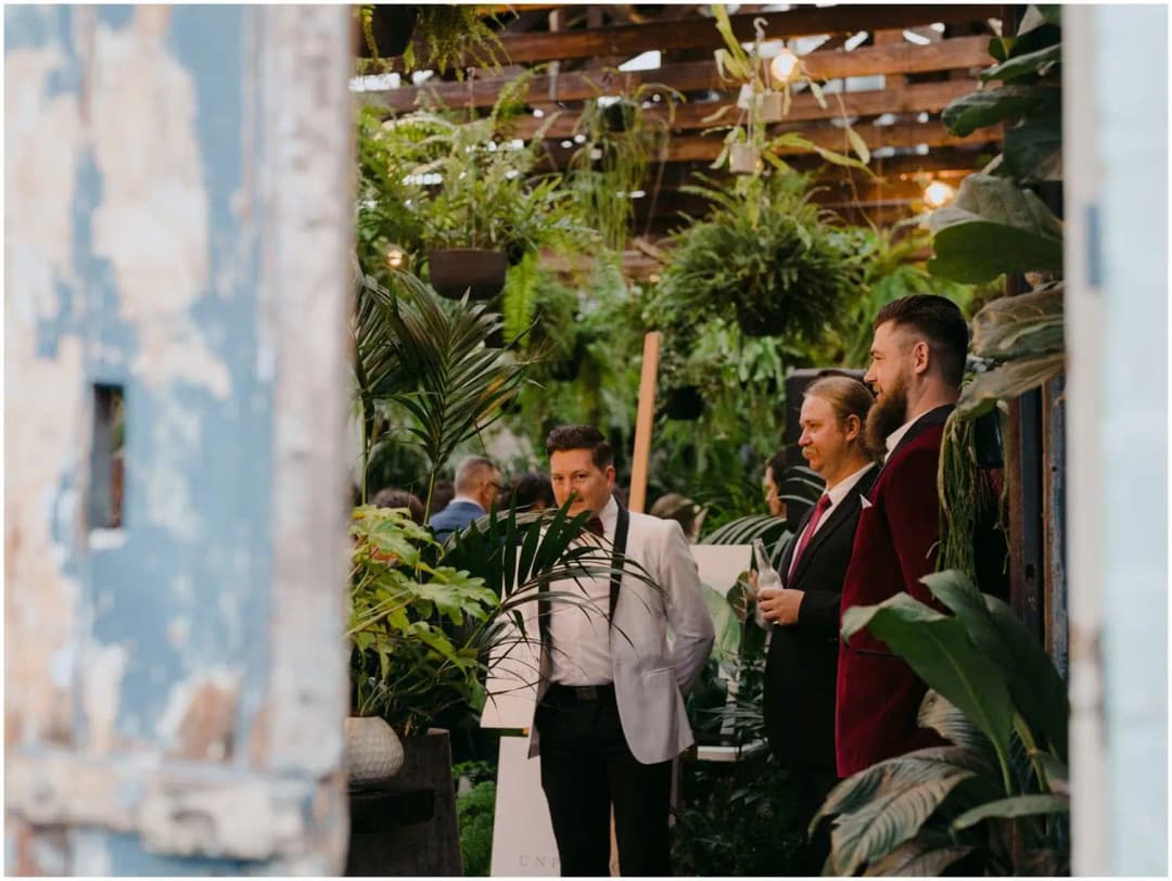 Men waiting amid dense greenery, viewed through a venue doorway