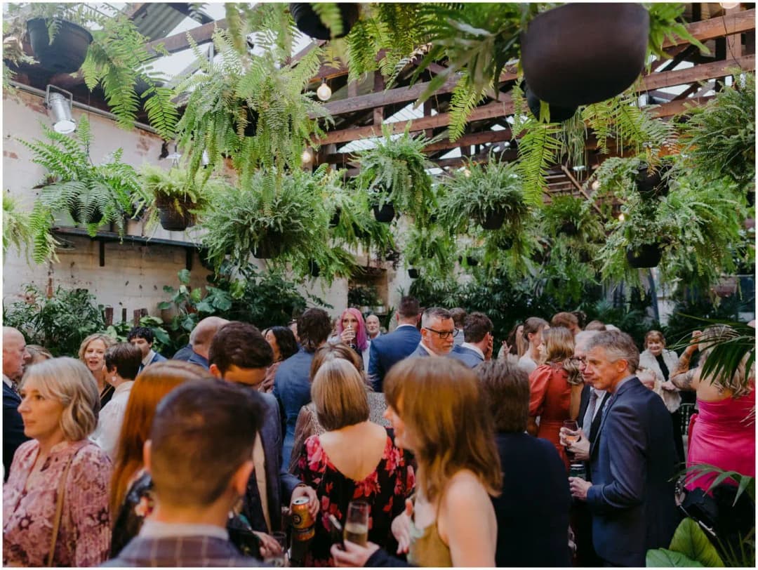 Wedding guests gathering beneath hanging plants and exposed roof beams
