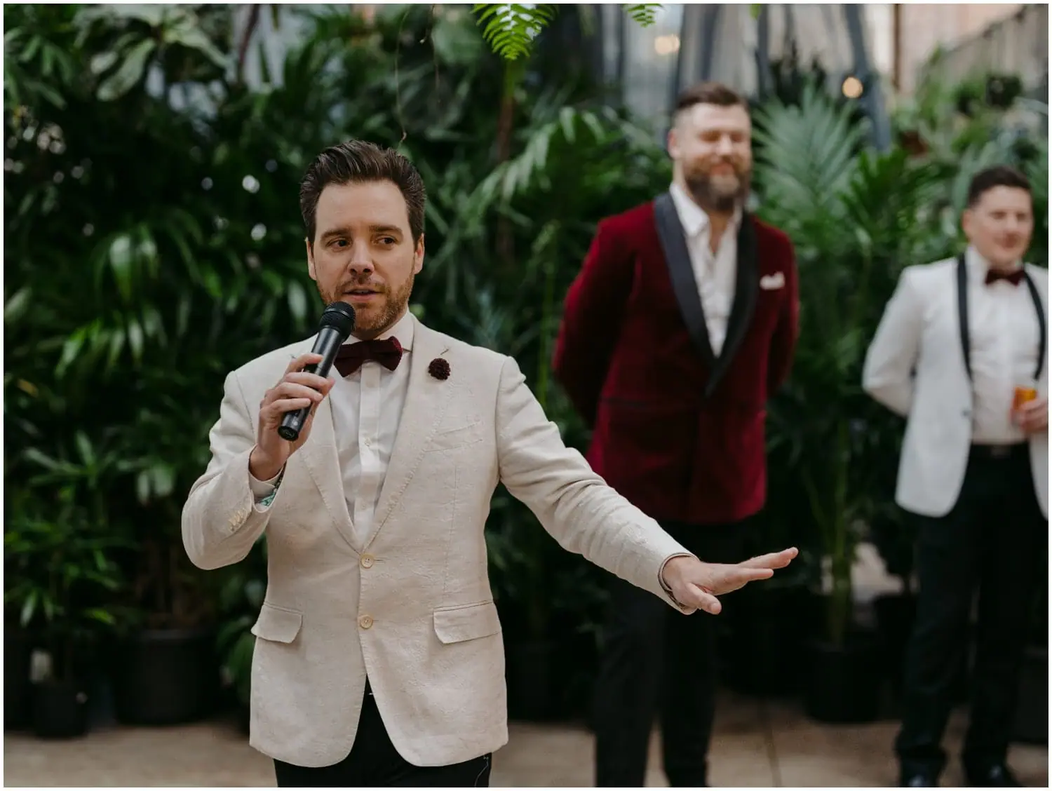 Man in a white jacket speaking into a microphone among leafy plants