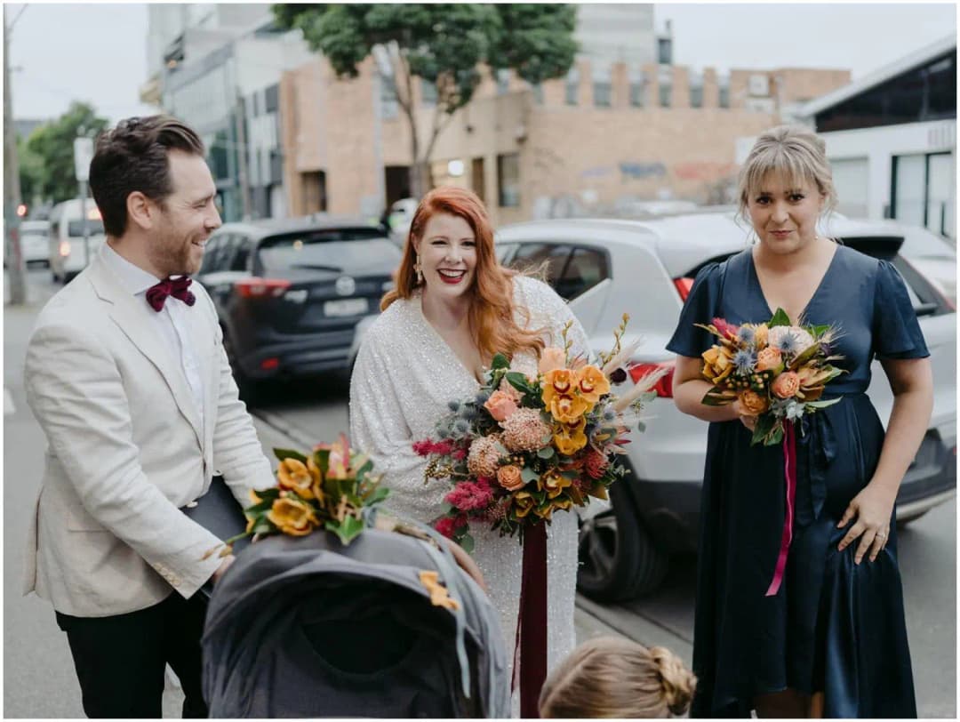 Bride standing with two companions and a pushchair on a city footpath