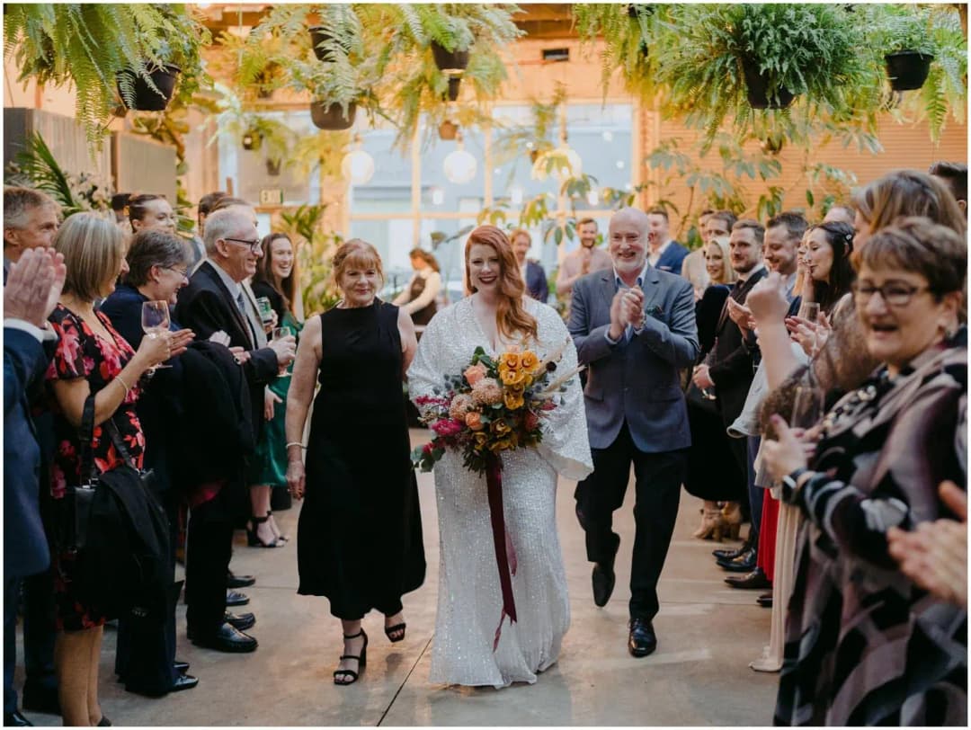 Bride walking between two companions as standing guests applaud