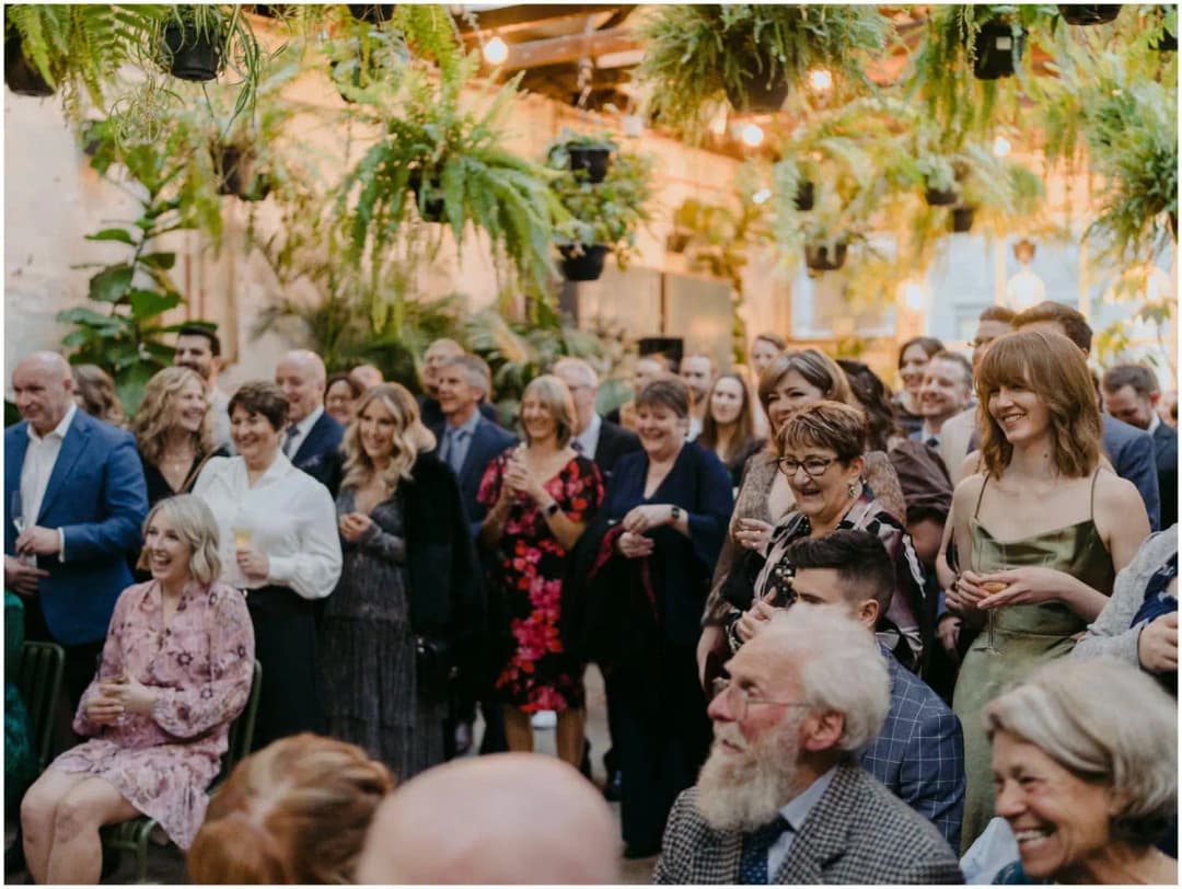 Wedding guests laughing beneath hanging ferns and warm ceiling lights
