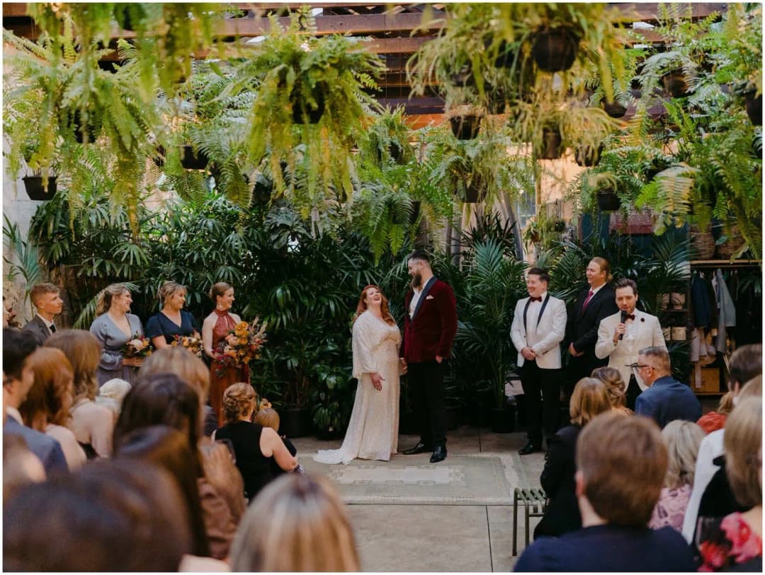 Wide view of the wedding ceremony beneath hanging plants and exposed beams