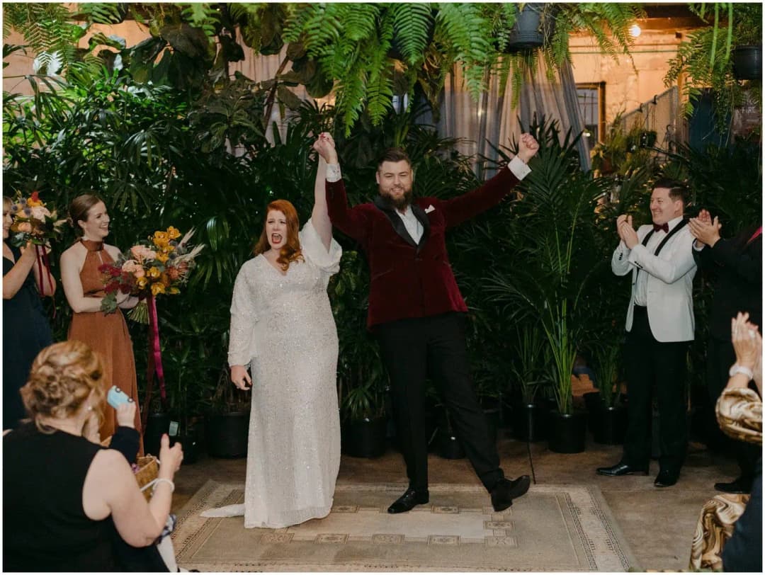 Groom raising both arms beside the smiling bride as guests applaud