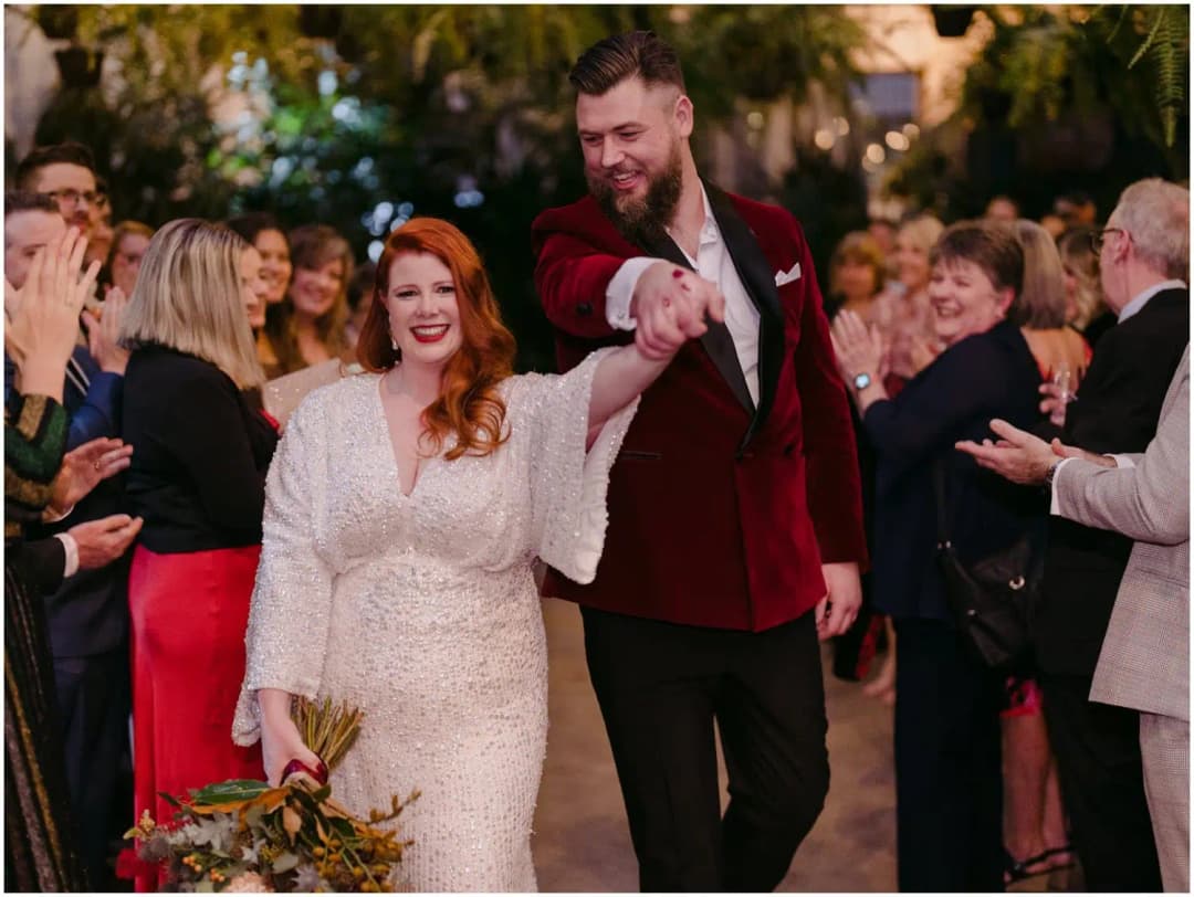 Groom raising the bride's hand as they walk together between cheering guests