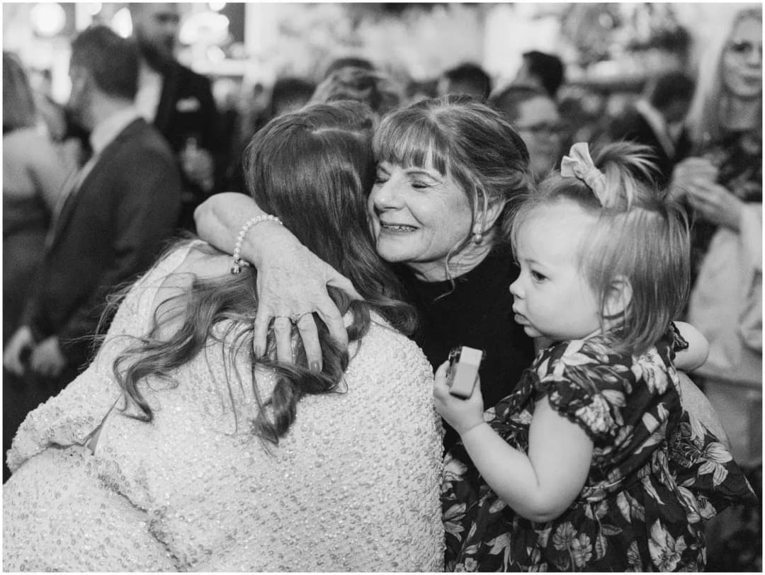 Black-and-white photograph of the bride hugging a woman holding a young child