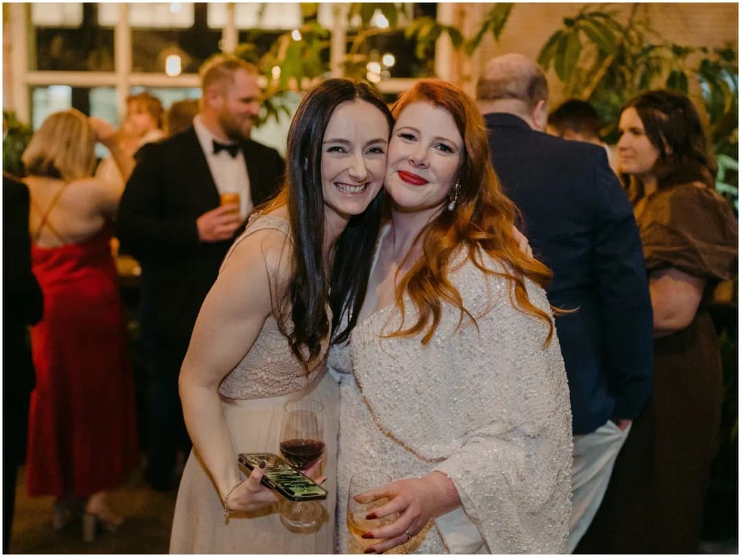 Bride and a friend leaning together and smiling with drinks