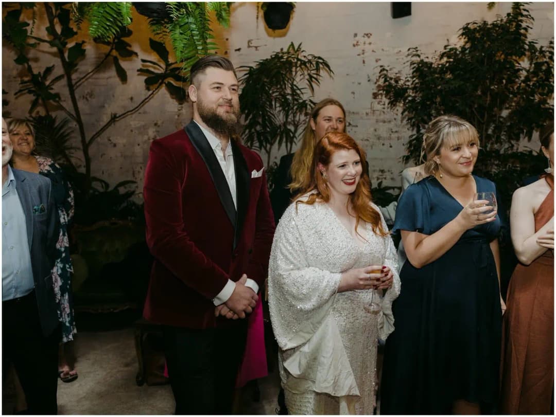 Bride and groom listening beside a woman holding a wine glass