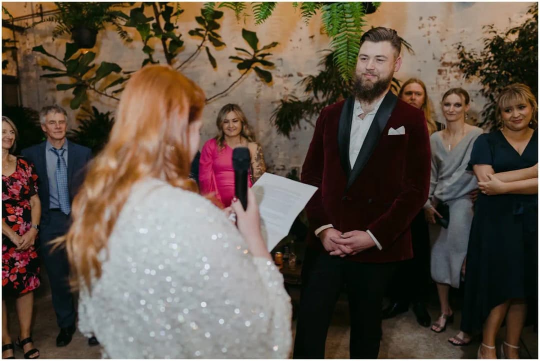 Bride holding a microphone and reading from paper while the groom listens