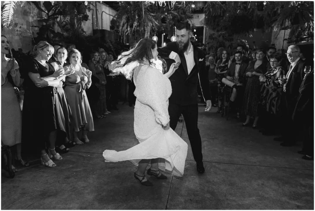 Black-and-white photograph of the bride twirling beside the groom as guests watch