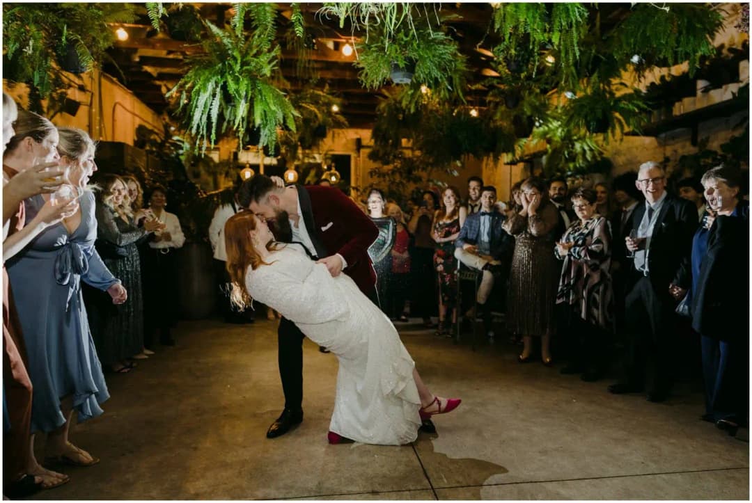 Groom dipping the bride during their dance beneath hanging plants