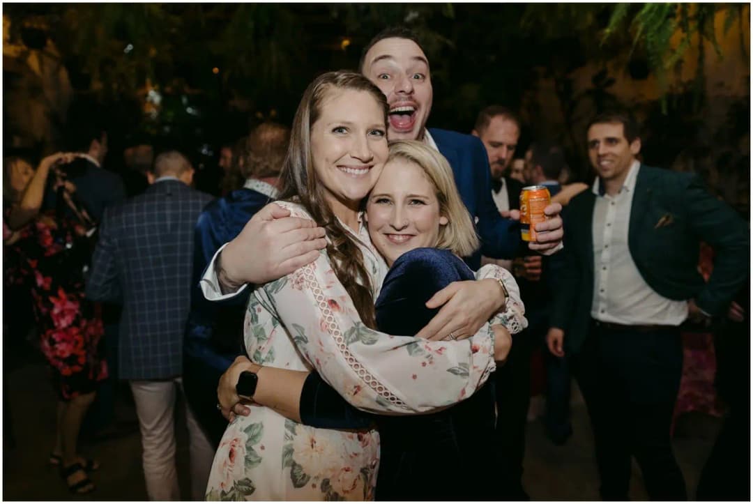 Three guests hugging and smiling together at the reception