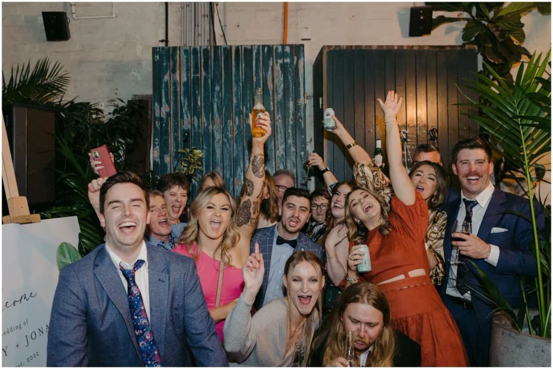 Group of wedding guests cheering and raising drinks toward the camera