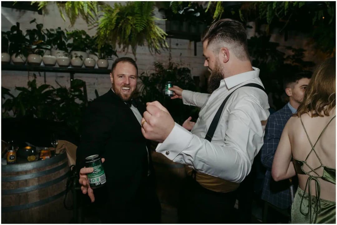 Groom dancing in a white shirt and braces beside a laughing guest