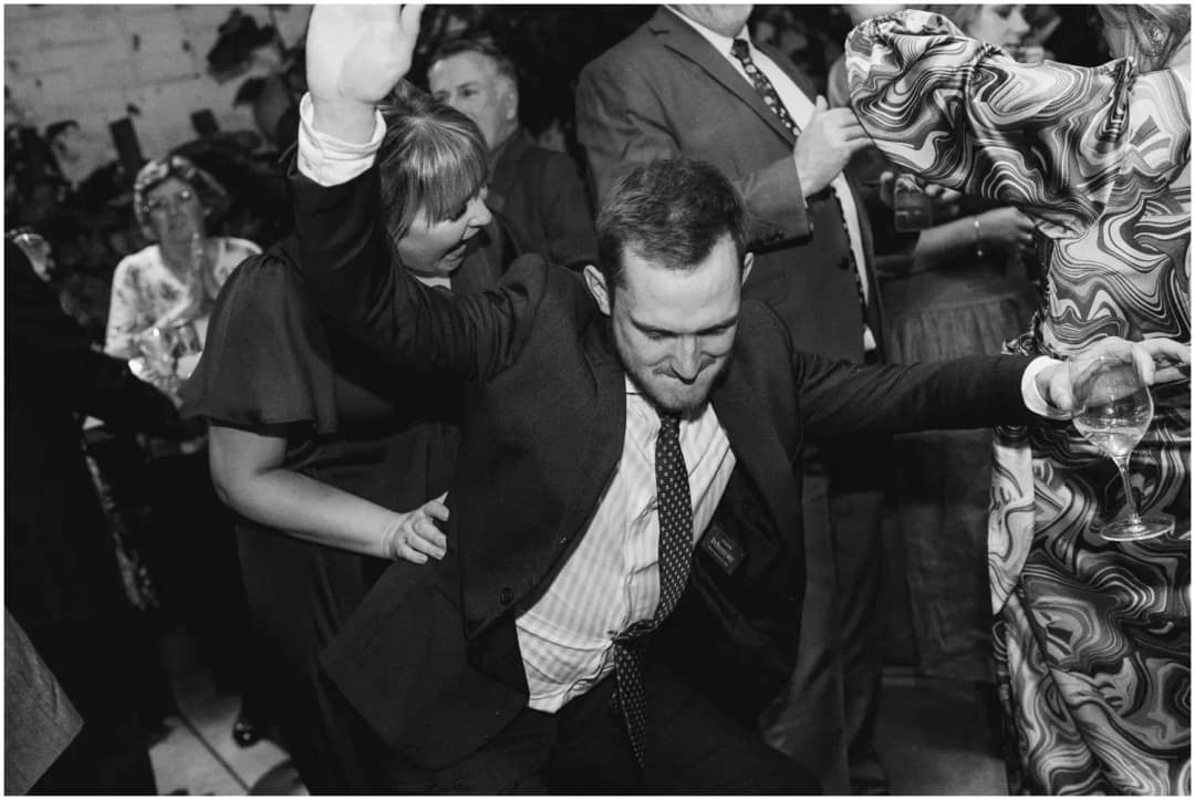 Black-and-white photograph of a guest dancing with both arms raised