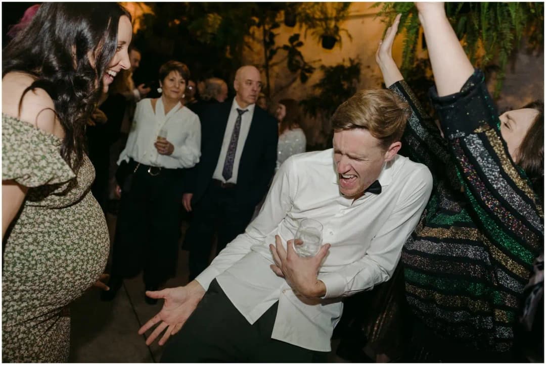 Guest leaning backward and gesturing while others dance around him