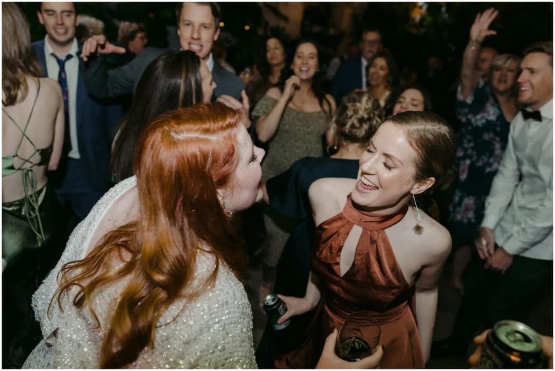 Bride and a friend laughing face to face on the crowded dance floor