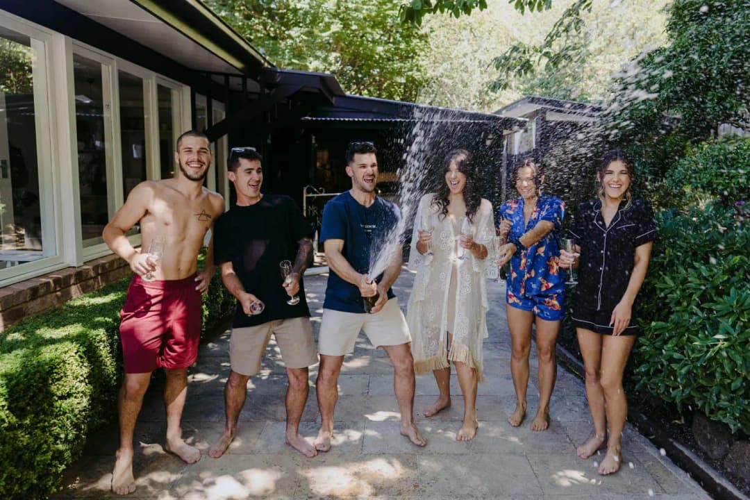 Wedding party laughing outdoors as a bottle sprays sparkling wine