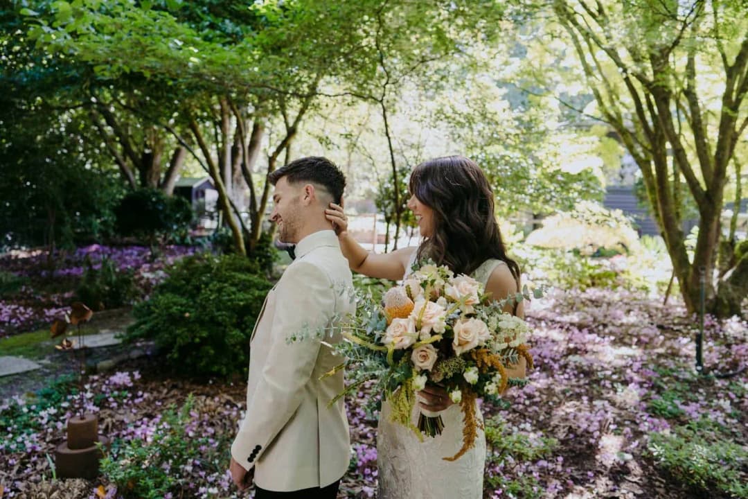Bride resting her hand on the groom's shoulder beneath flowering trees