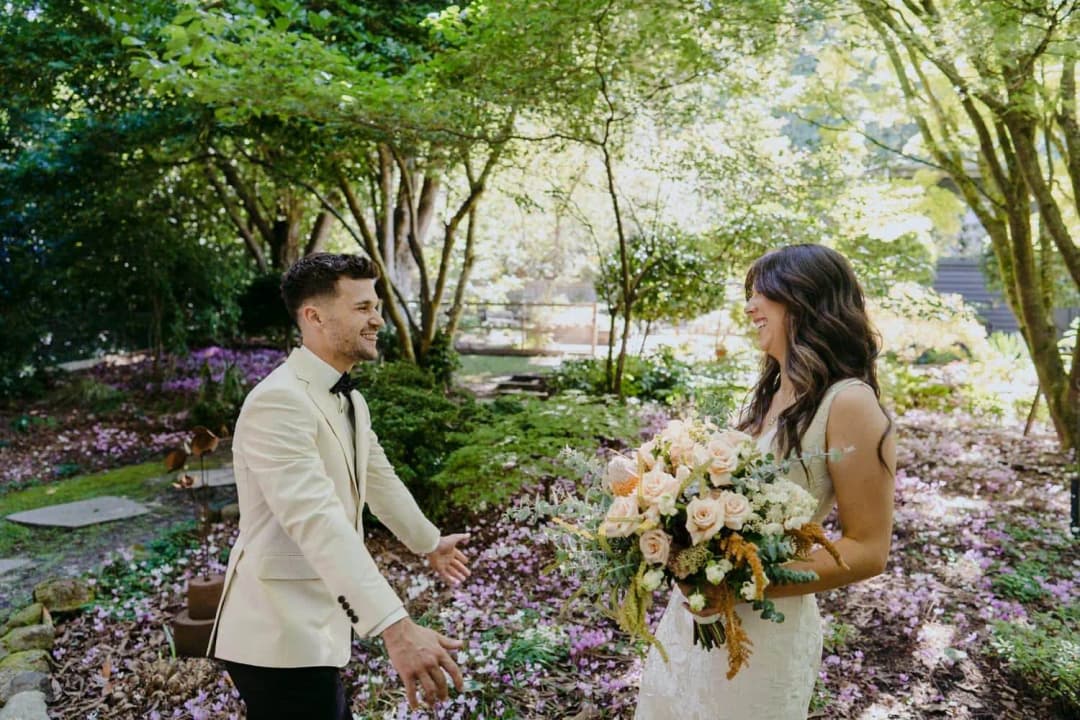 Groom turning toward the bride with his arms open in the garden