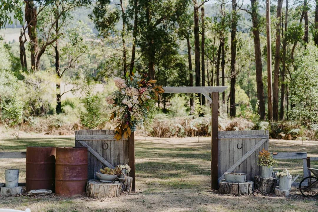 Rustic timber ceremony entrance decorated with flowers, barrels and watering cans