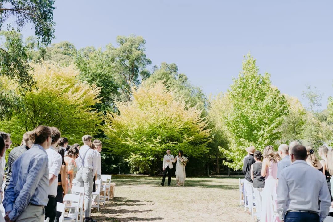Bride and groom approaching the outdoor ceremony between standing guests