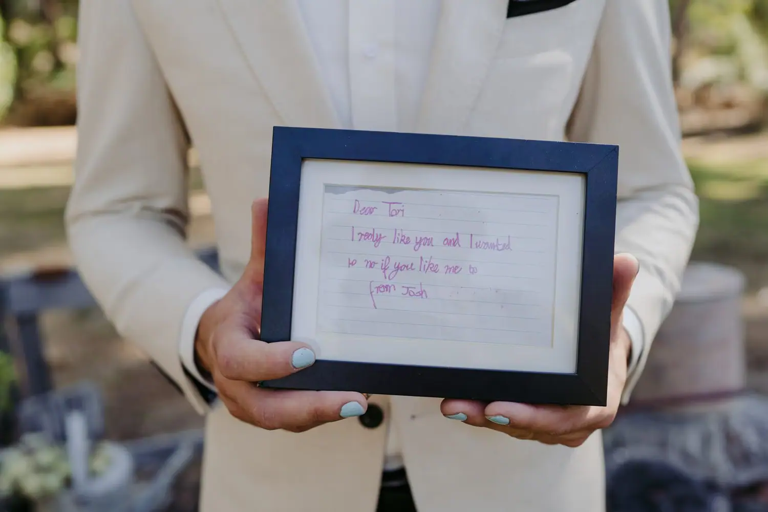 Person in a cream jacket holding a framed handwritten love note