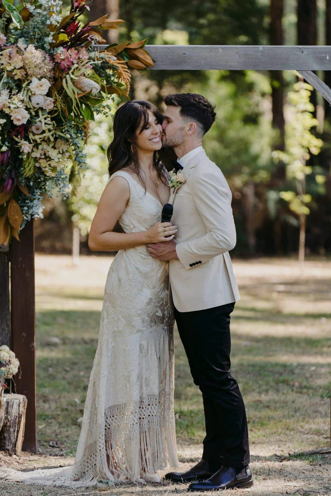 Bride and groom kissing beneath a flower-decorated timber entrance