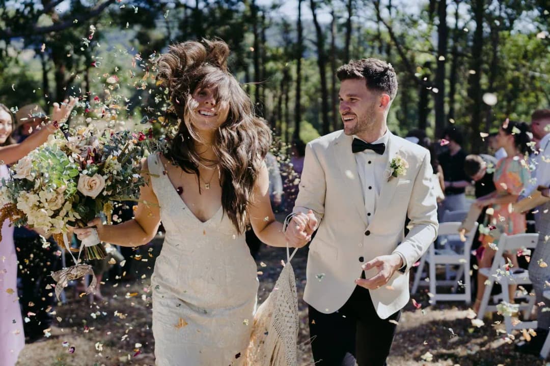 Bride and groom laughing as colourful confetti falls around them