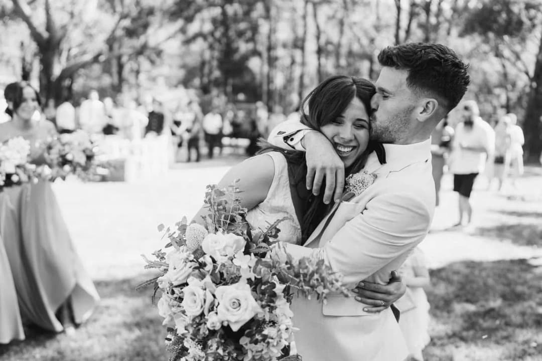 Black and white photograph of the groom kissing the smiling bride's forehead