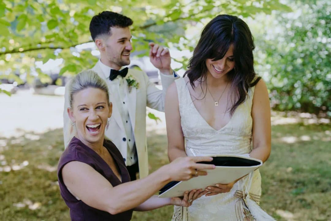 Couple smiling beside the celebrant while holding a dark folder