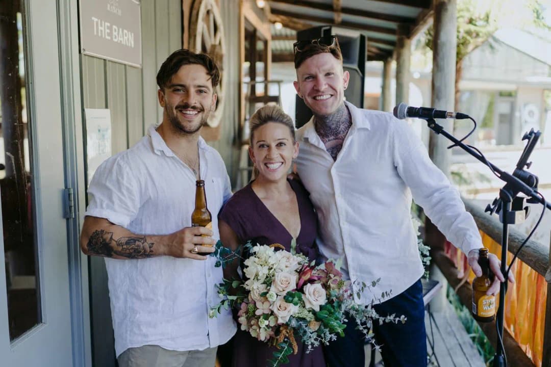Two guests posing with the celebrant outside the barn beside musical equipment
