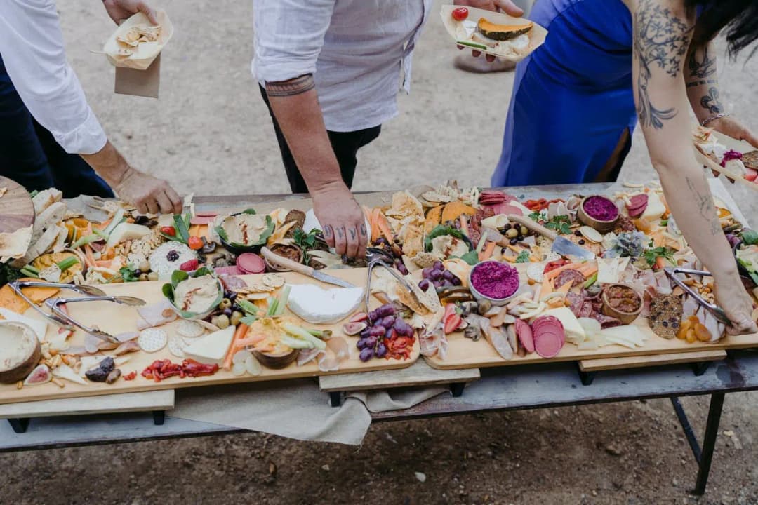 Guests serving themselves from a large grazing table of fruit, cheese and cold meats