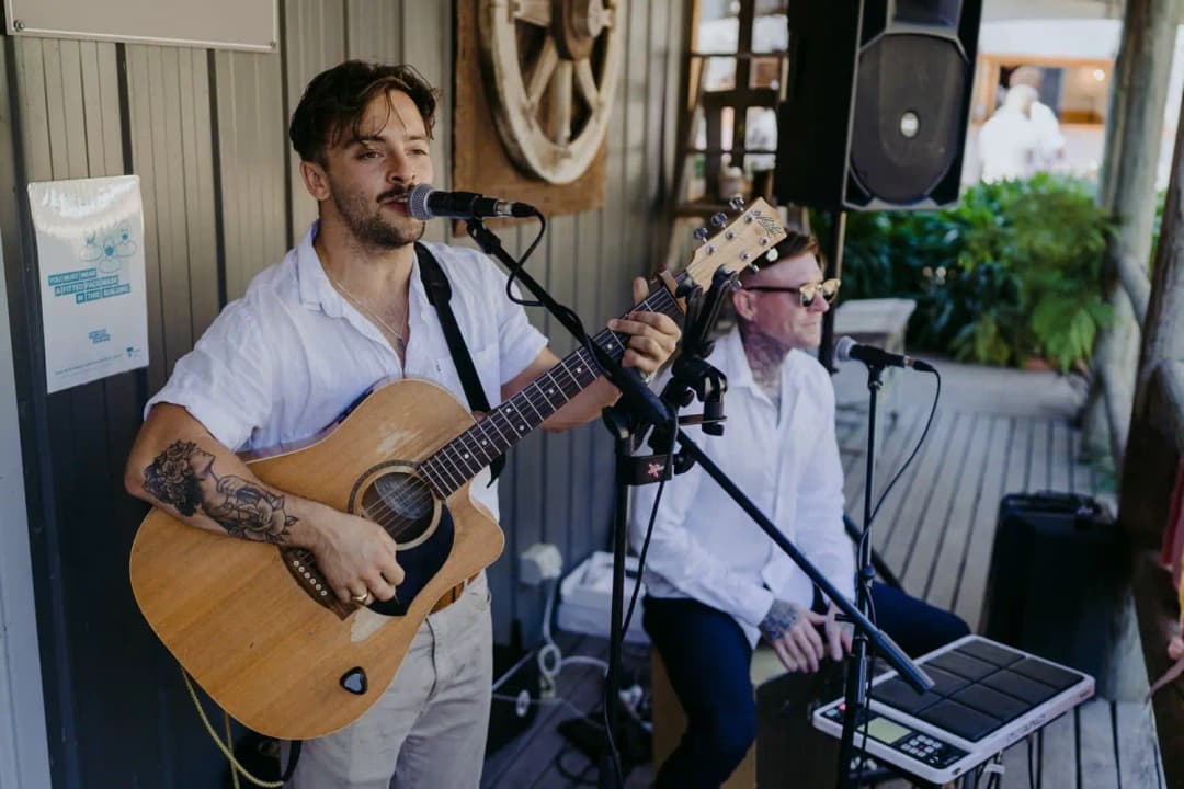 Guitarist singing beside another musician outside the barn