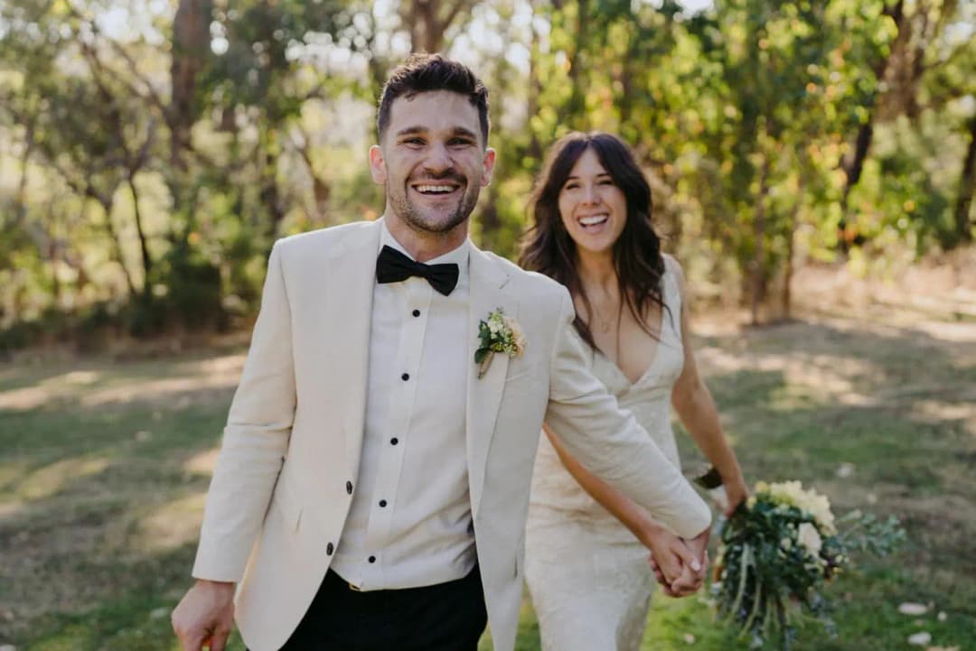 Bride and groom smiling while walking together through woodland
