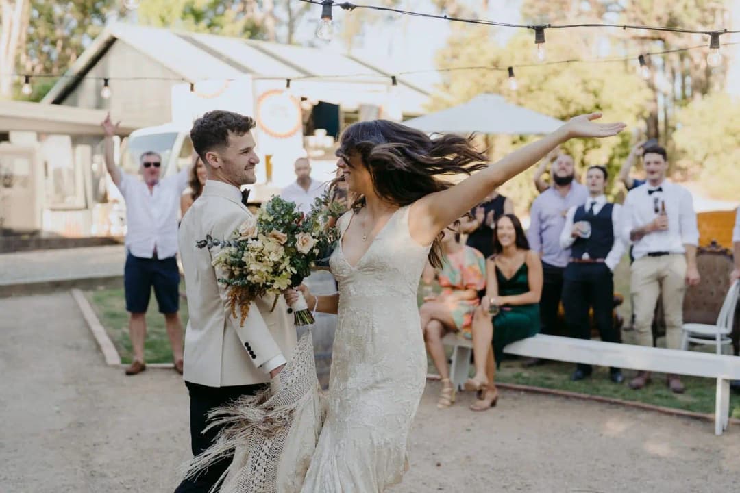 Bride raising her arm while turning beside the groom as guests cheer