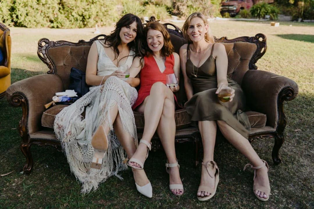 Bride and two guests sitting together on an antique sofa outdoors