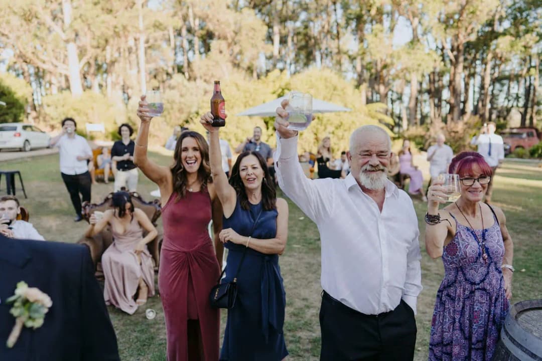 Guests raising drinks toward the couple outside the reception barn