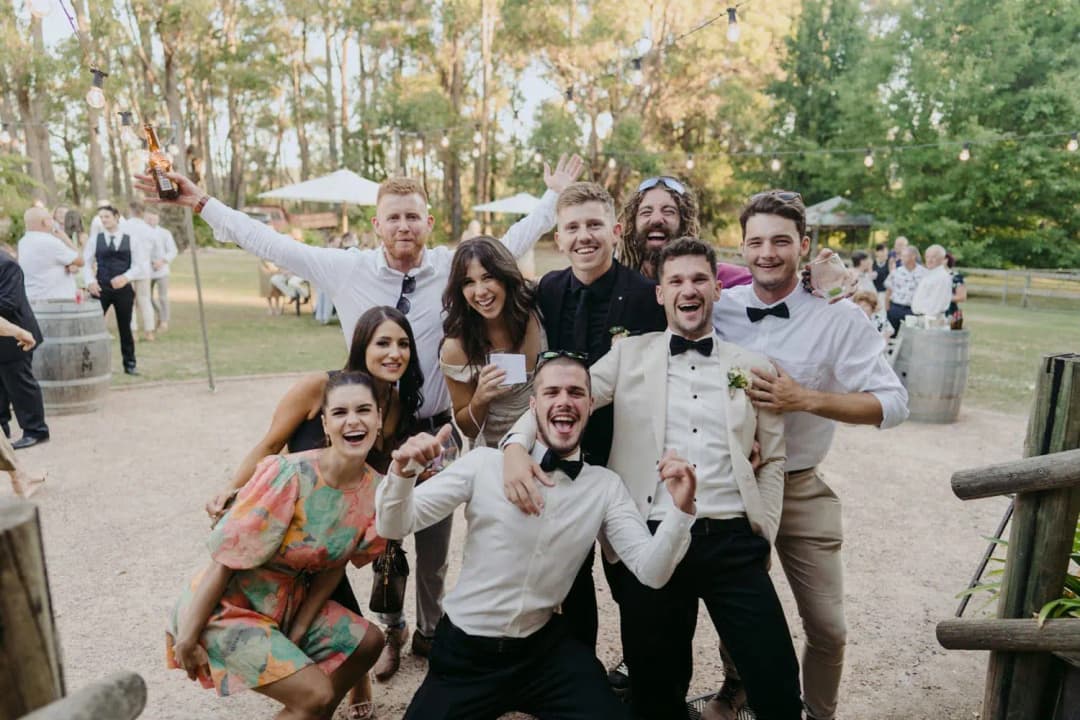 Bride and groom posing with a group of smiling guests outdoors
