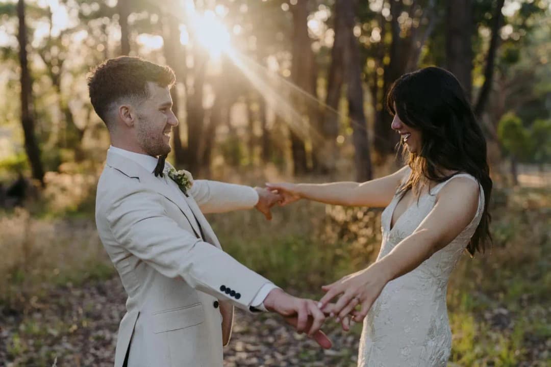 Bride and groom holding both hands as evening sunlight filters through trees
