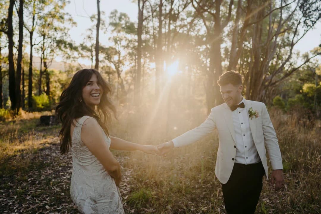 Bride smiling while holding the groom's hand in sunlit woodland