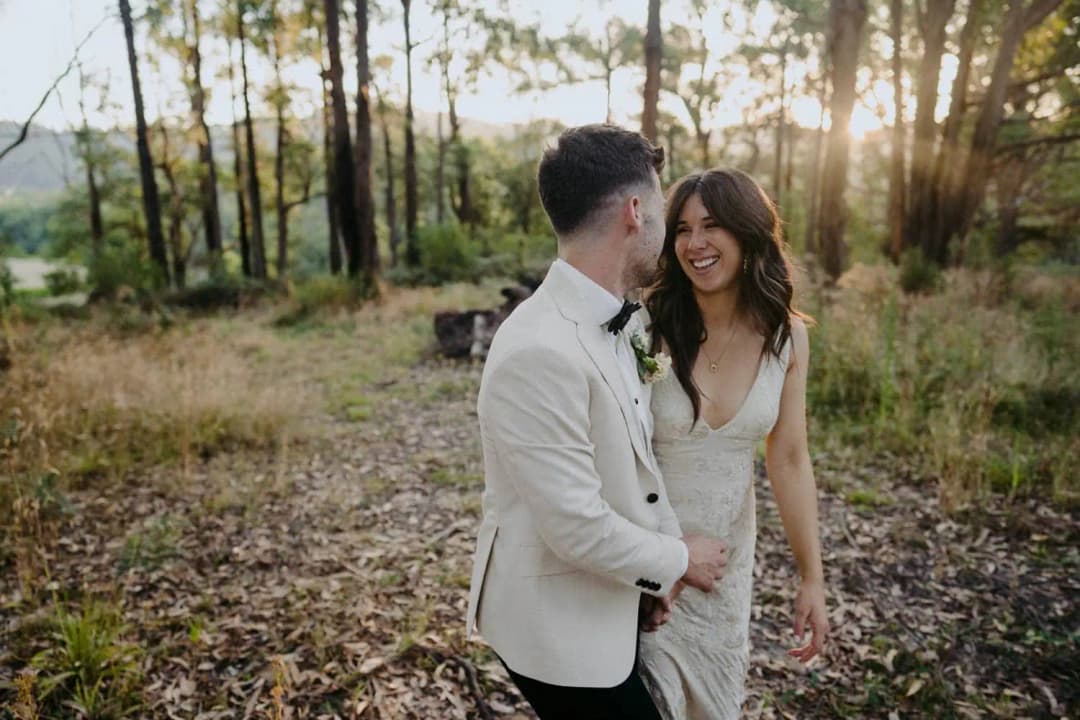 Bride and groom smiling closely together among sunlit trees
