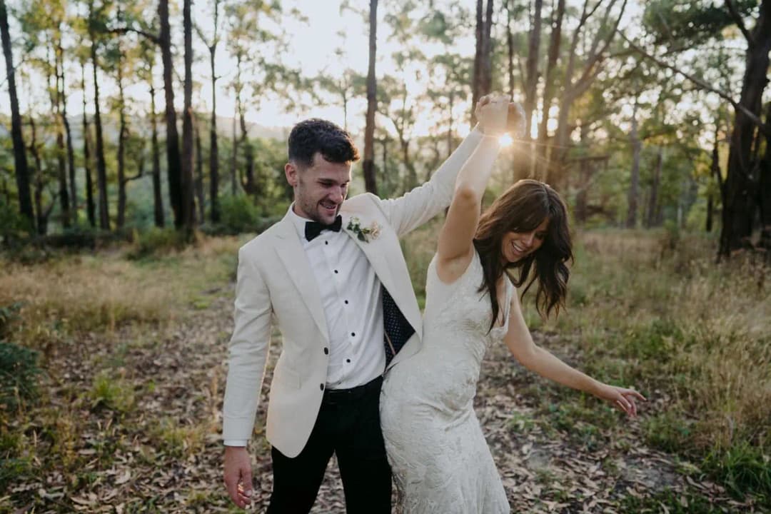 Groom holding the bride's hand above her head as she twirls in woodland