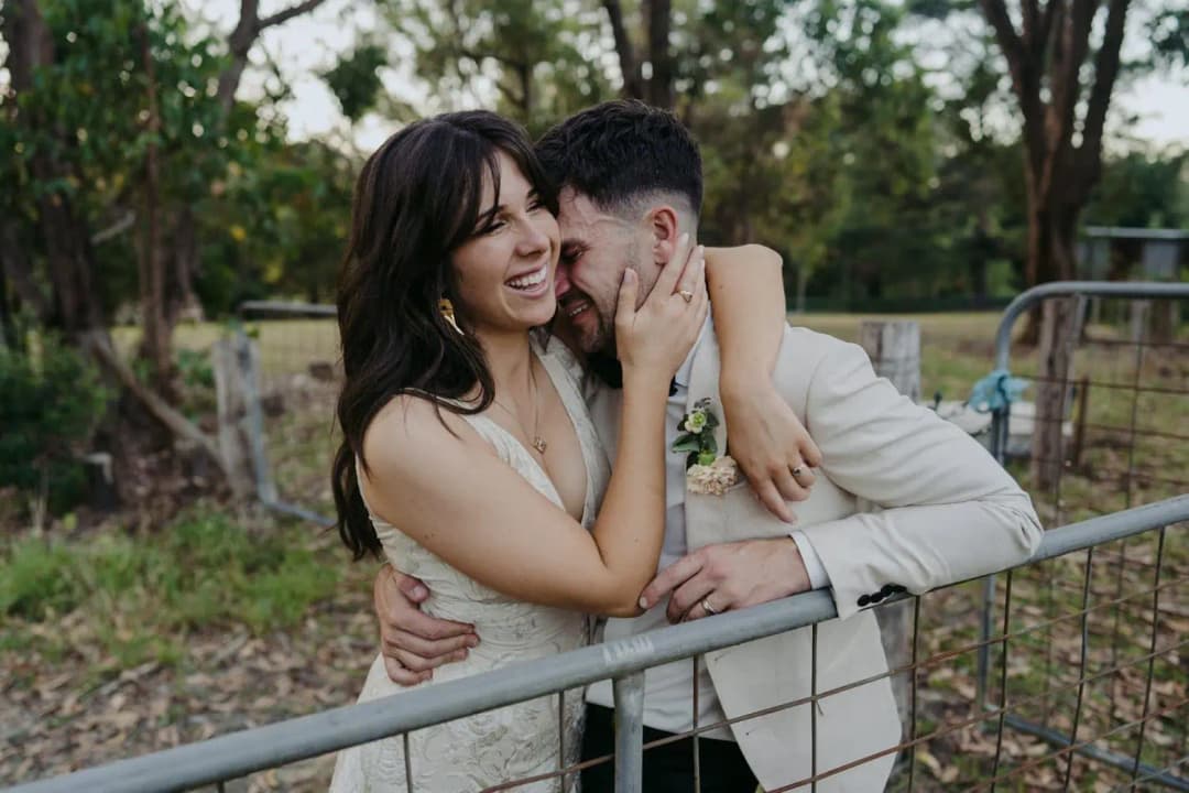 Bride laughing while embracing the groom beside a metal farm gate