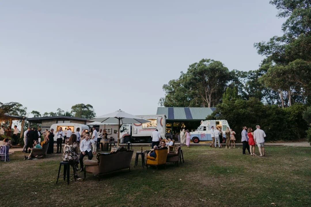 Guests relaxing outside among food vans and cabin buildings at dusk