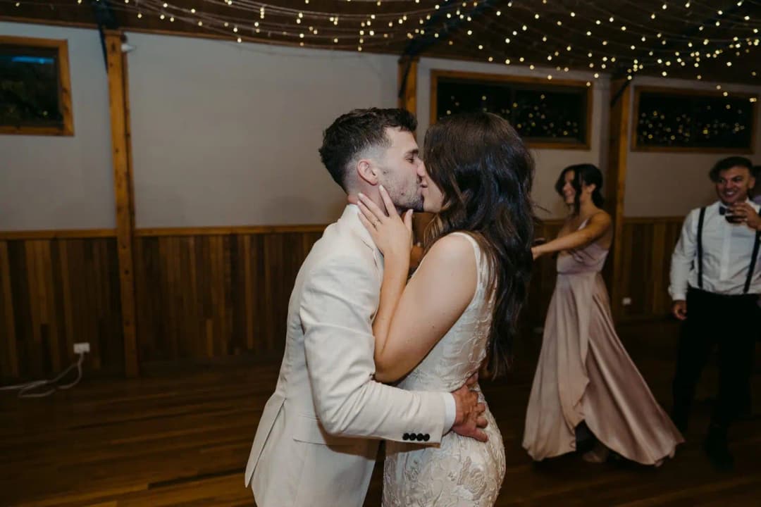 Bride and groom kissing on the dance floor beneath fairy lights