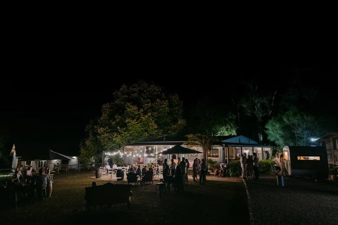 Reception barn and guests illuminated among trees after dark