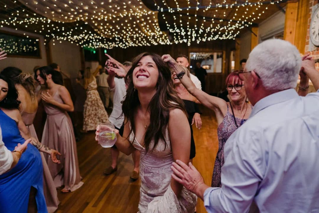 Smiling guest dancing with a drink beneath a ceiling of fairy lights