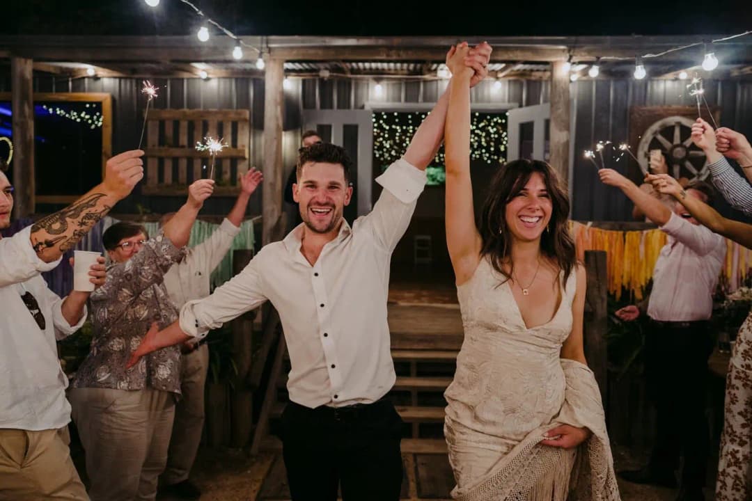 Bride and groom raising their joined hands as guests cheer outdoors at night