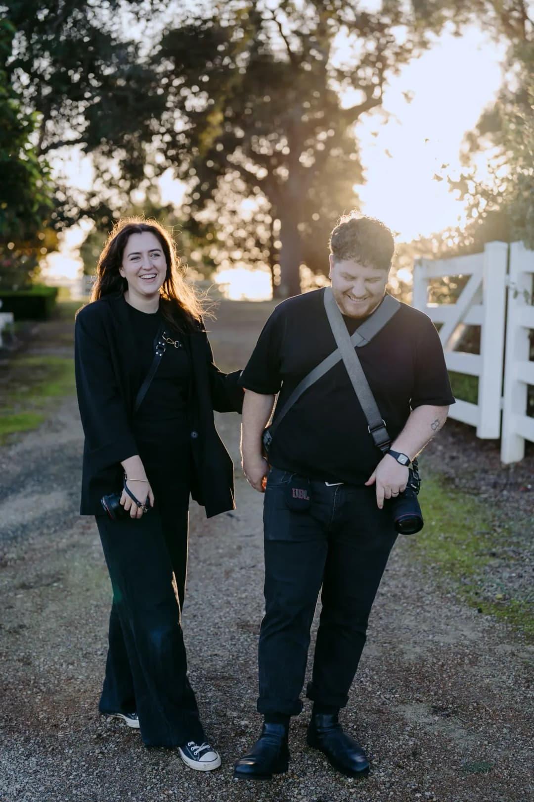 Two camera-carrying photographers standing on a garden path at sunset.
